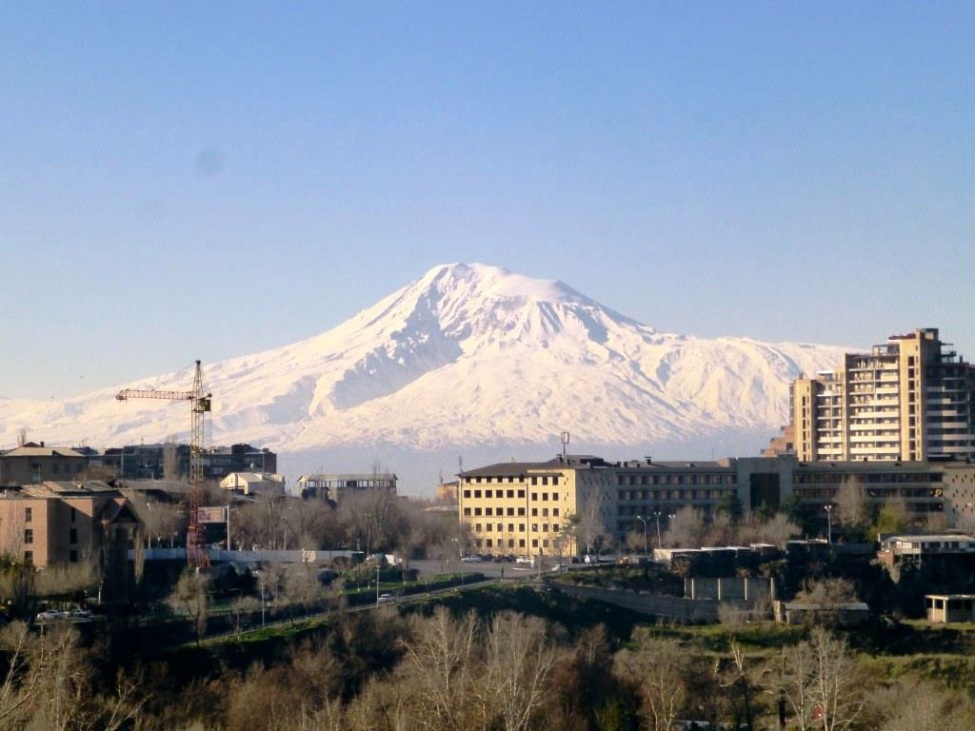 Blick auf einen Schneebedeckten Berg. Im Vordergrund Häuser der Stadt Jerewan