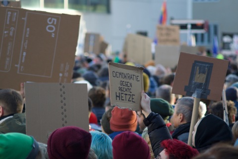 demonstrierende Menschenmenge, auf Pappe geschriebenes Schild „Demokratie gegen Hetze“
